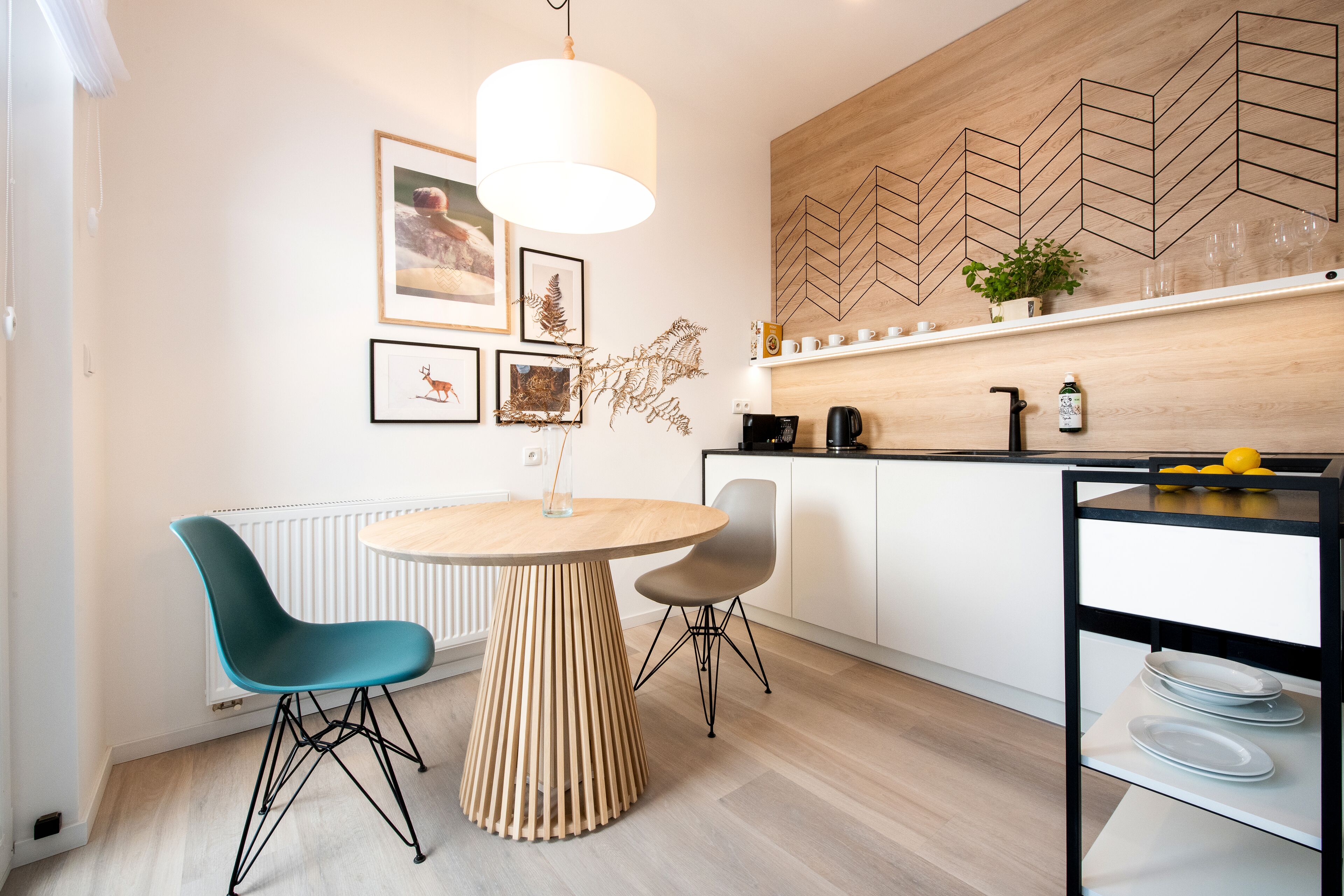 A modern kitchen with a wooden herringbone backsplash, a round wooden table, two chairs, and a hanging pendant light.