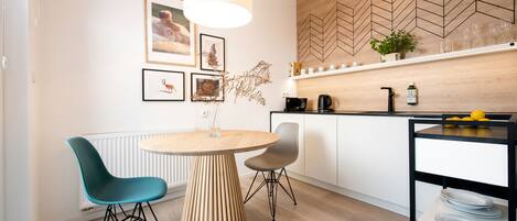 A modern kitchen with a wooden herringbone backsplash, a round wooden table, two chairs, and a hanging pendant light.