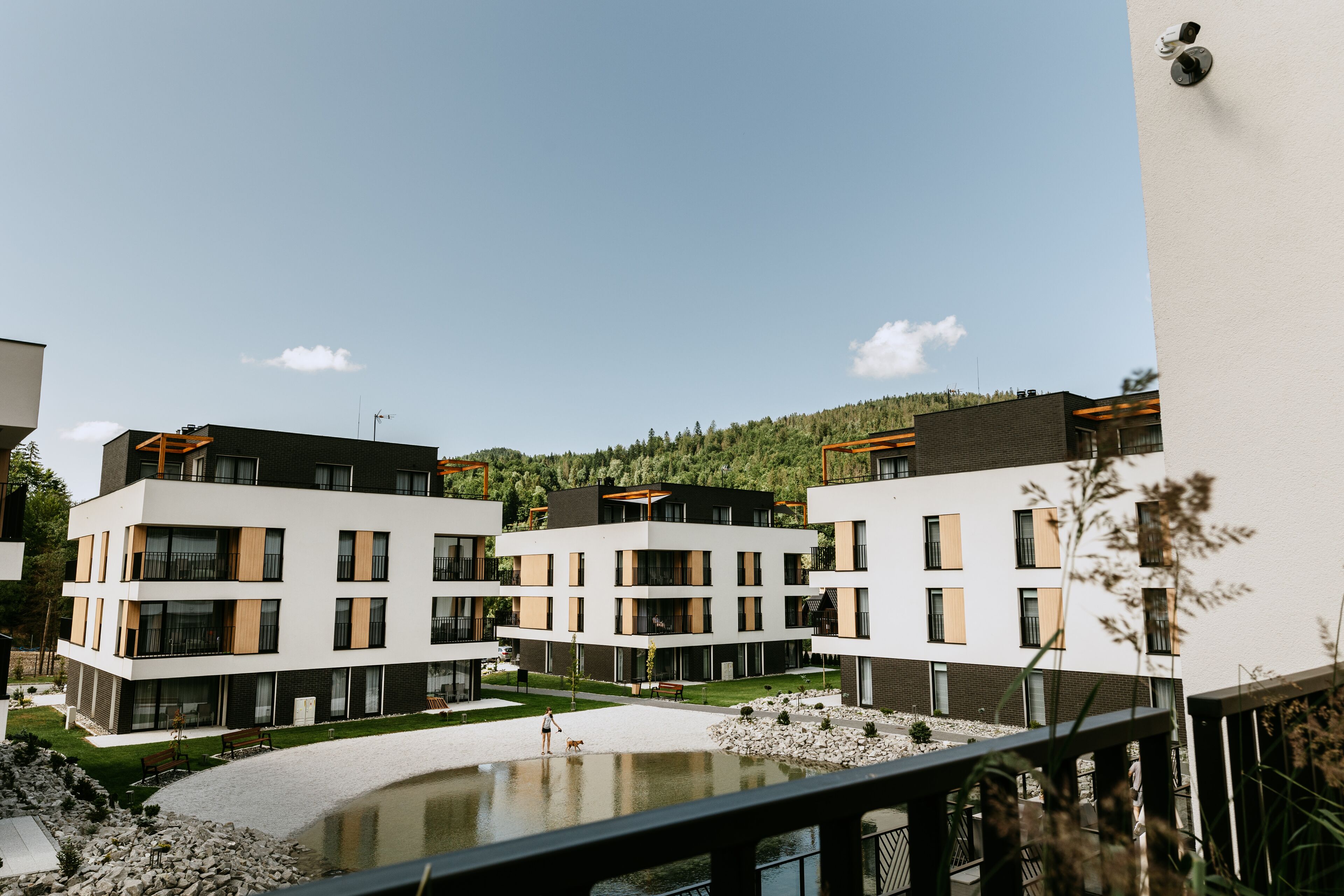 Un moderno complejo de apartamentos con varios edificios, un patio central y un pequeño estanque.