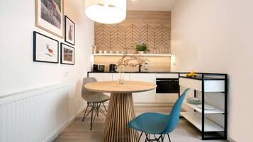 A modern kitchen with a round wooden table, two chairs, a hanging light fixture, and framed pictures on the wall.
