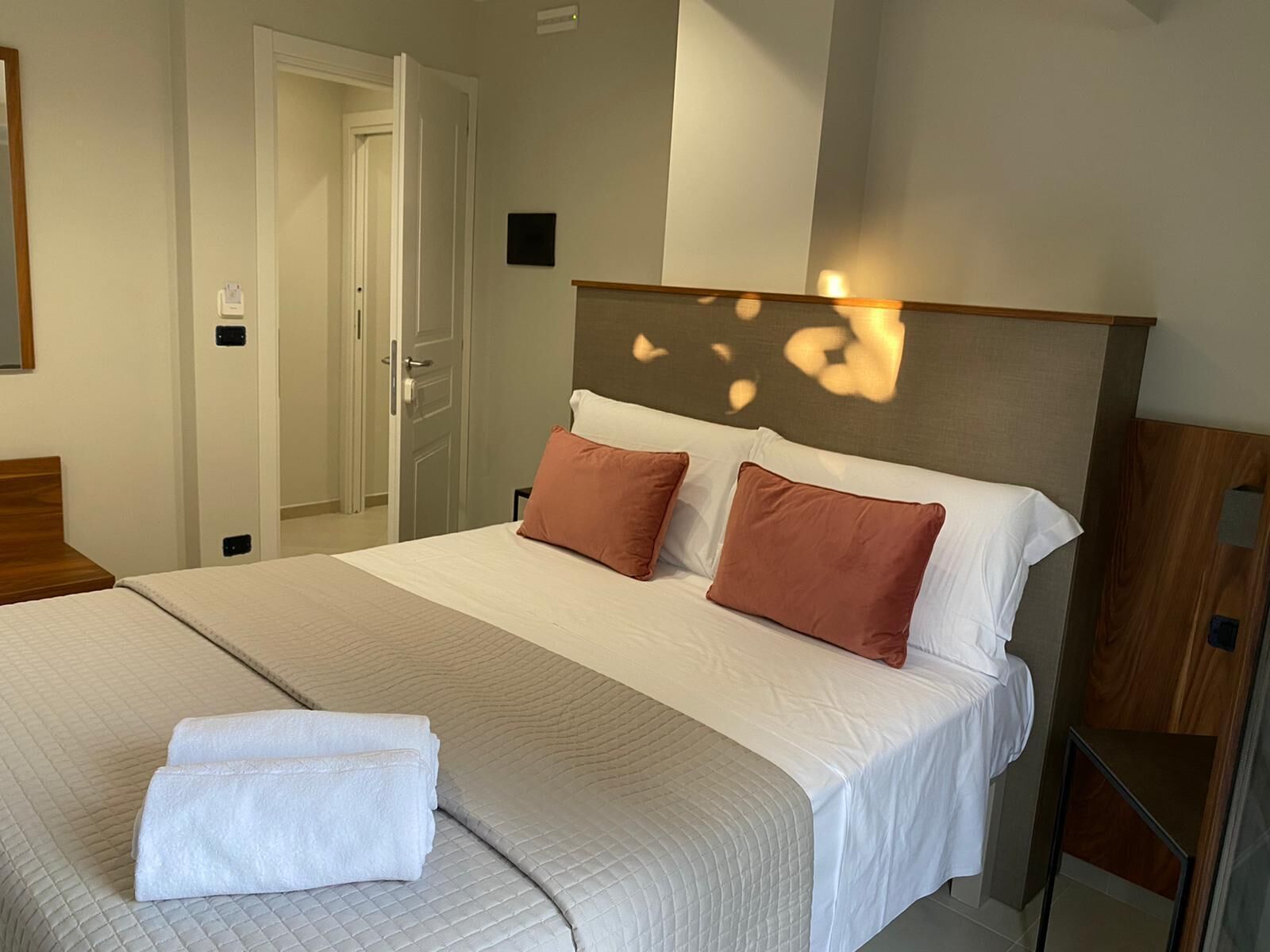 A neatly made bed with a quilted bedspread, two pillows, and folded towels on the side.