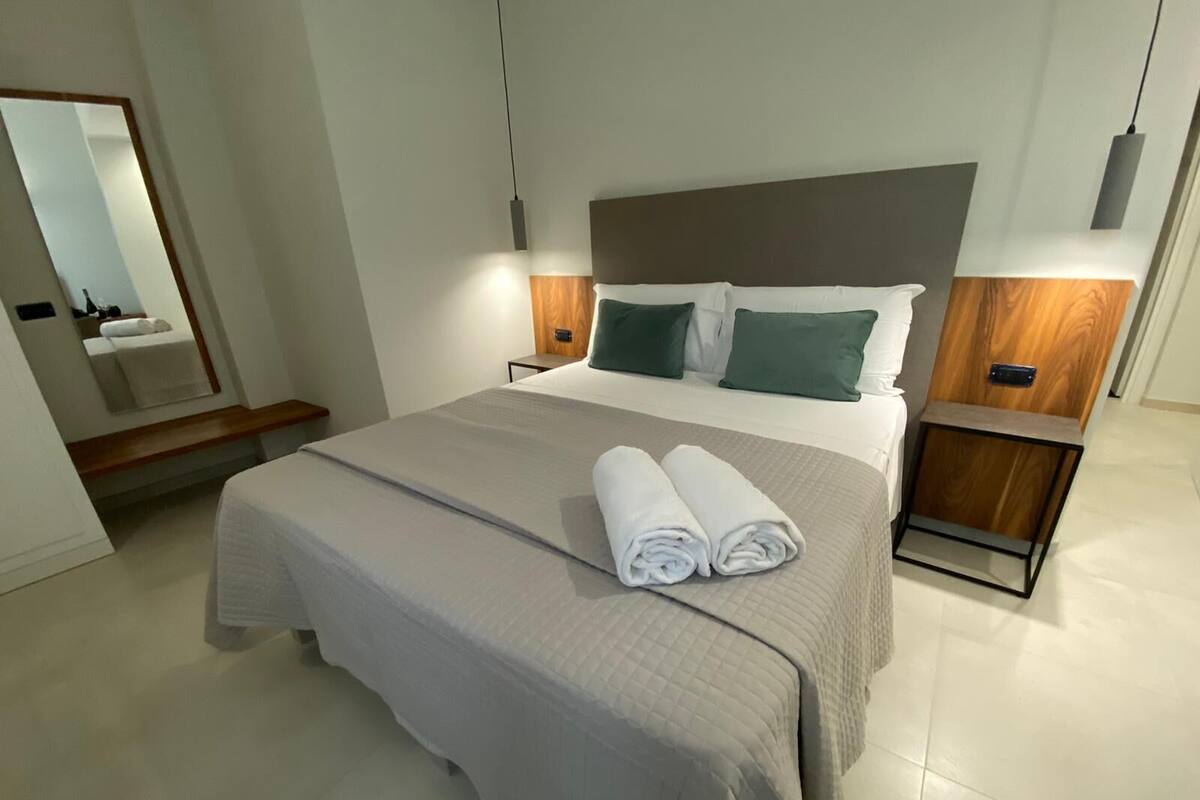 Une chambre d’hôtel moderne avec un grand lit, deux tables de chevet, une tête de lit en bois et un miroir.