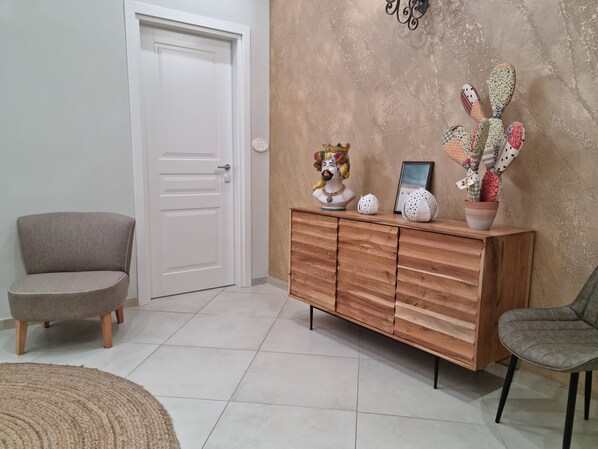 A room with a wooden cabinet, a grey armchair, a white door, and a textured wall.
