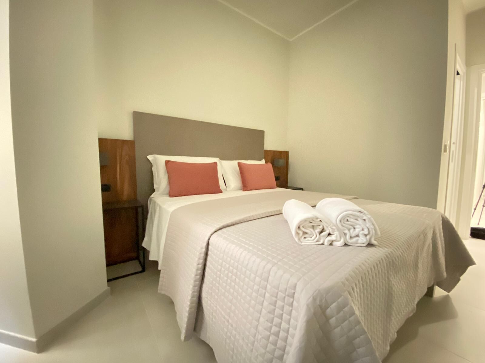 A neatly made bed with a quilted cover, two pillows, and a rolled towel on the side.