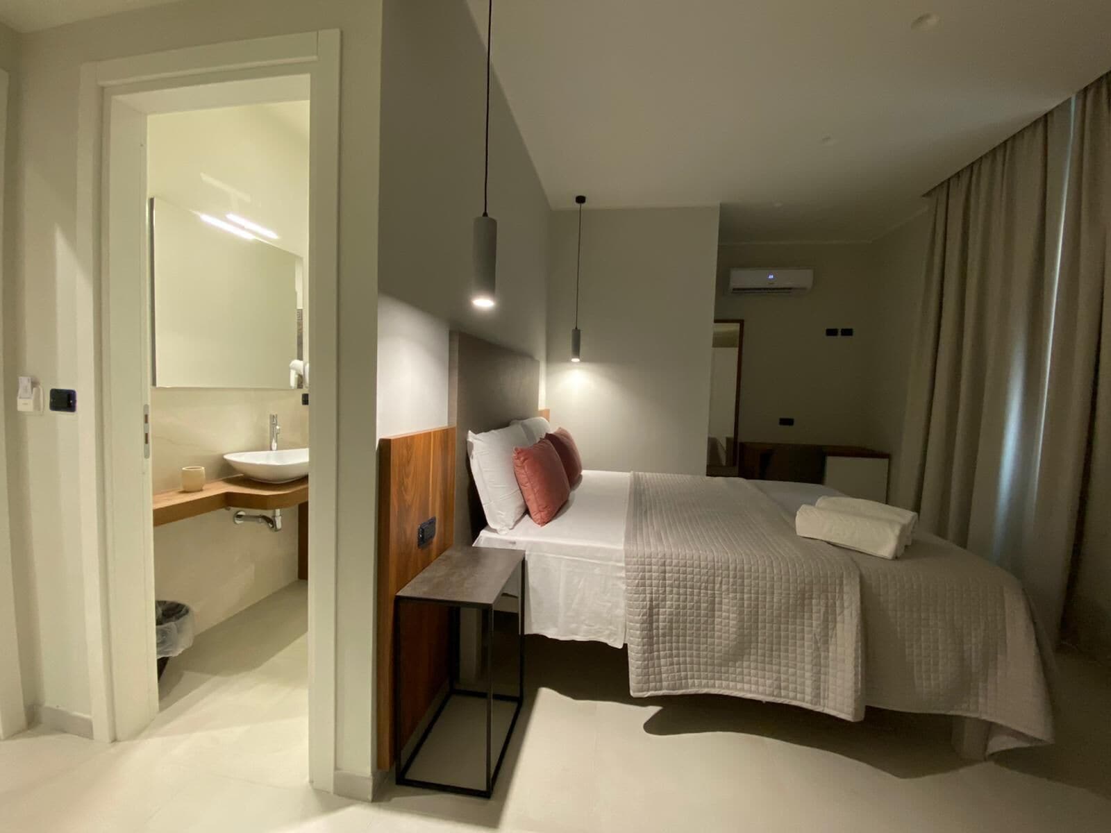 Une chambre d’hôtel moderne, équipée d’un lit, d’une table de chevet et d’une salle de bain visible à travers une porte ouverte.