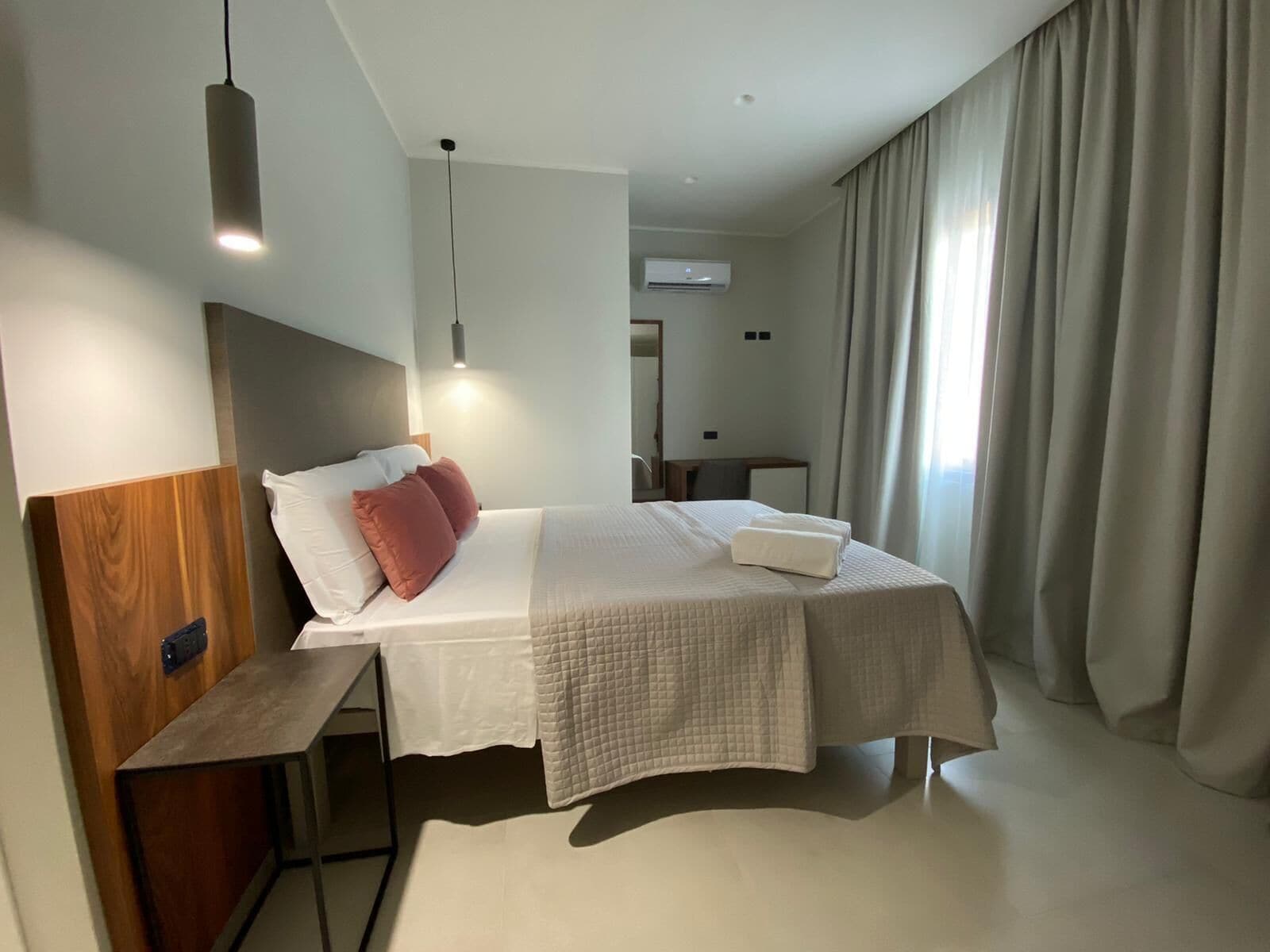 A modern hotel room with a bed, bedside table, and a hanging light fixture.
