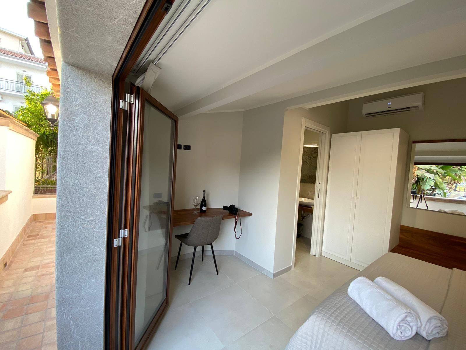 A hotel room with a bed, a desk, and a chair. There is a window with a view of the outside.