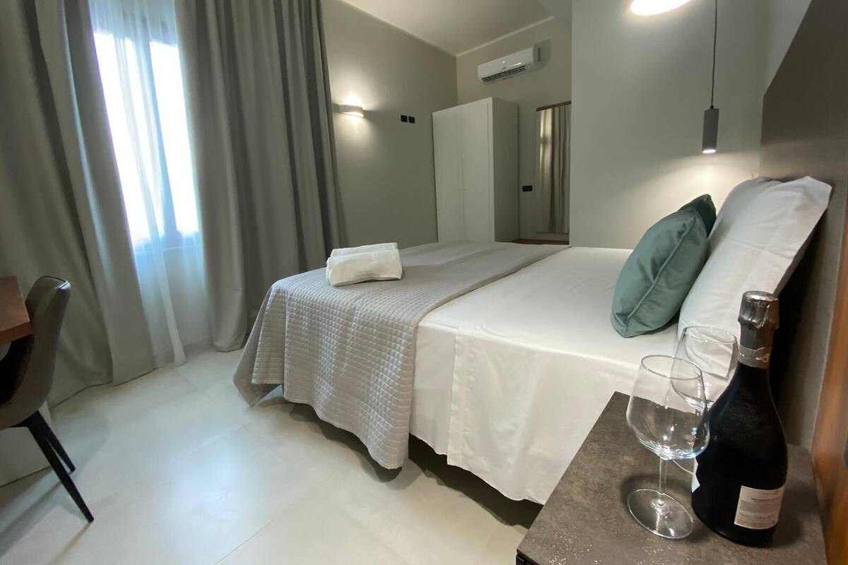 Une chambre d’hôtel avec un lit, un bureau, une chaise, une bouteille de vin et un verre.