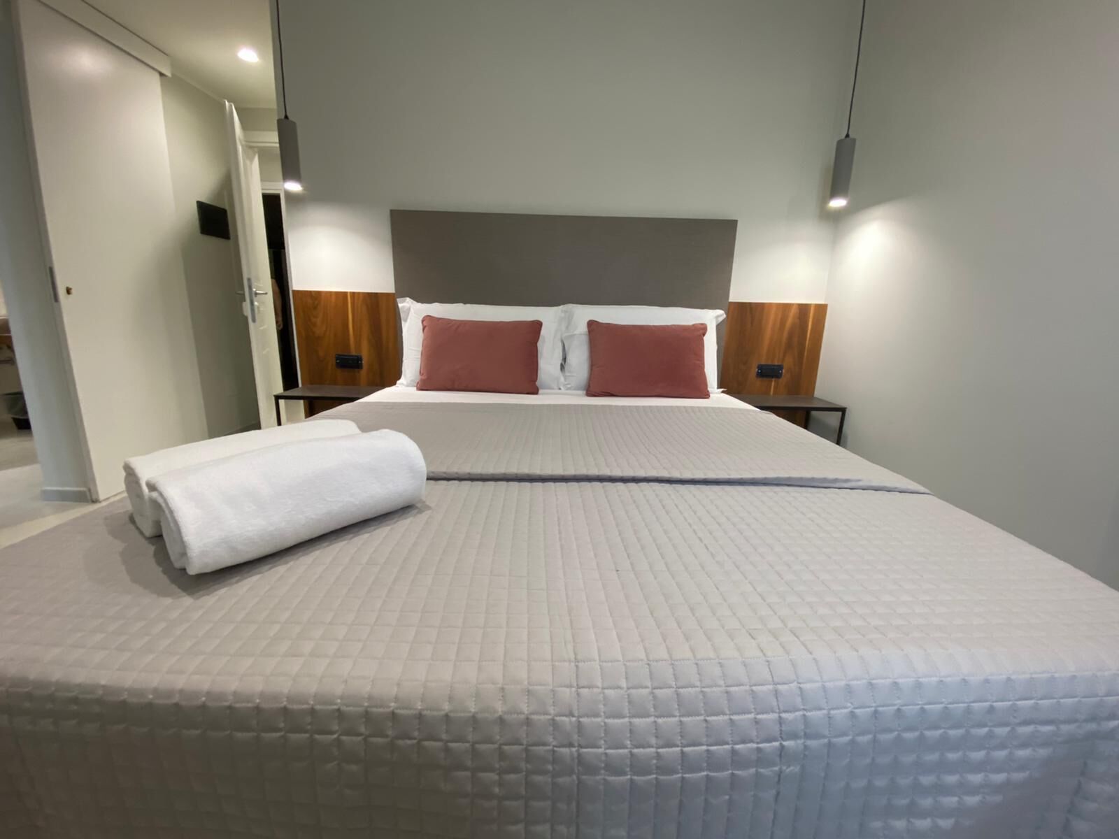 A neatly made bed with a rolled white towel, two wooden nightstands with lamps, and a headboard with two pillows.