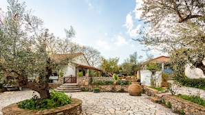 A courtyard with stone flooring, surrounded by trees and potted plants, leading to a building with a red-tiled roof. - The Fairytale House Seaside Retreat (Messini)