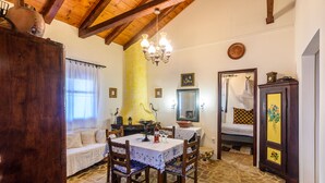 A dining area with a table, chairs, and a chandelier. There is a sofa with cushions and a window with curtains. A wooden cabinet and a mirror are also visible. - The Fairytale House Seaside Retreat (Messini)