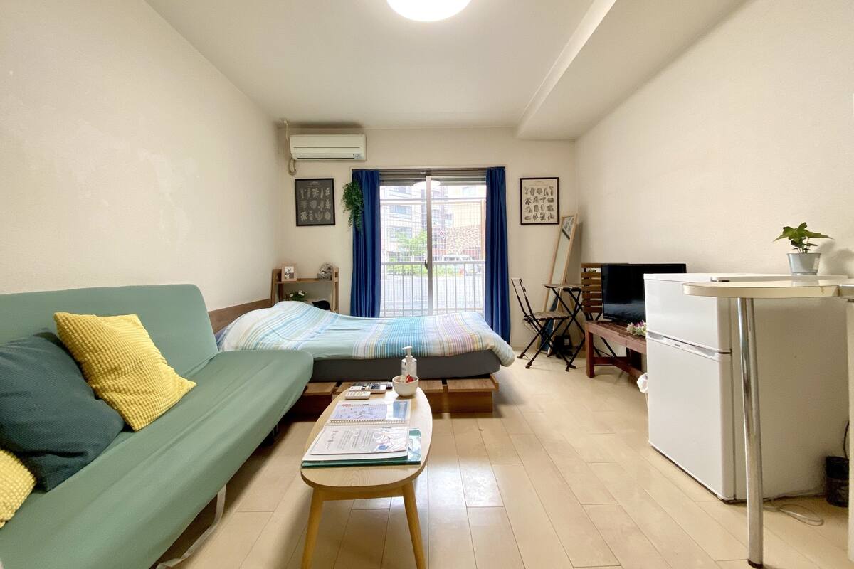 A compact living space with a bed, a sofa, a small table, a television, and a kitchenette.