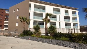 Un hôtel à plusieurs étages, doté d’un toit plat, de grandes fenêtres et d’un espace paysager agrémenté de palmiers.