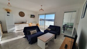 Un salon moderne avec deux canapés, une table basse, un téléviseur et un balcon équipé d’une table et de chaises.