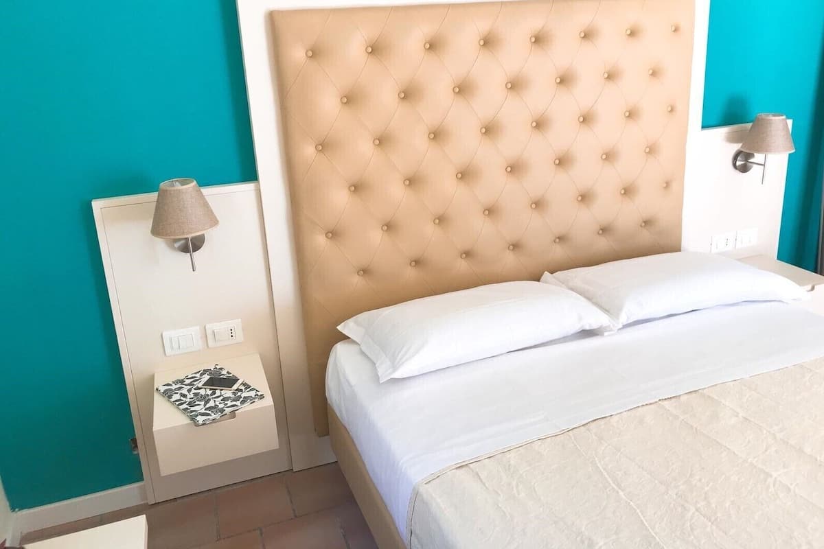 A neatly made bed with a tufted headboard, a bedside lamp, and a power outlet on the nightstand.