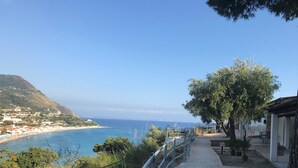 A coastal town with a beach, a hill with buildings, and a tree-lined pathway. - Hotel Marina del Capo (Ricadi)