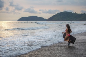 Une plage avec des vagues, une personne en bikini et, au loin, une colline boisée.