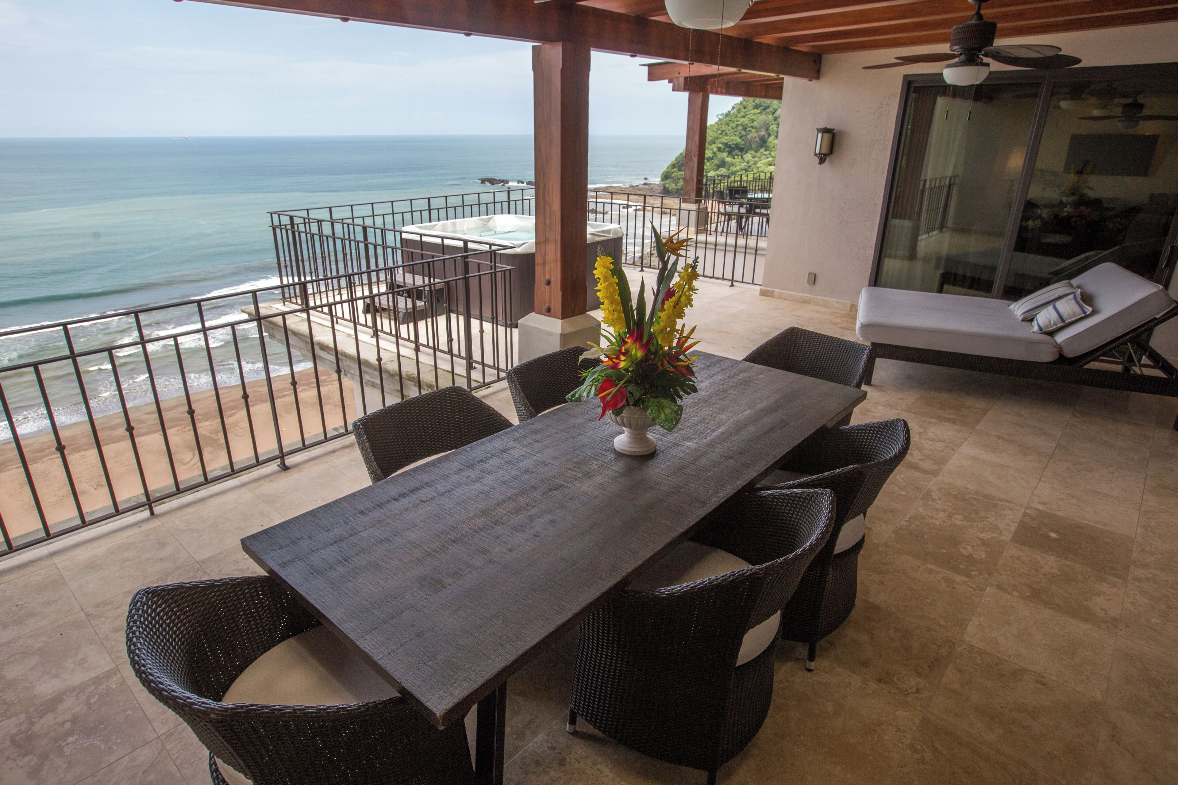 A balcony with a view of the ocean, a dining table with chairs, and a sofa.