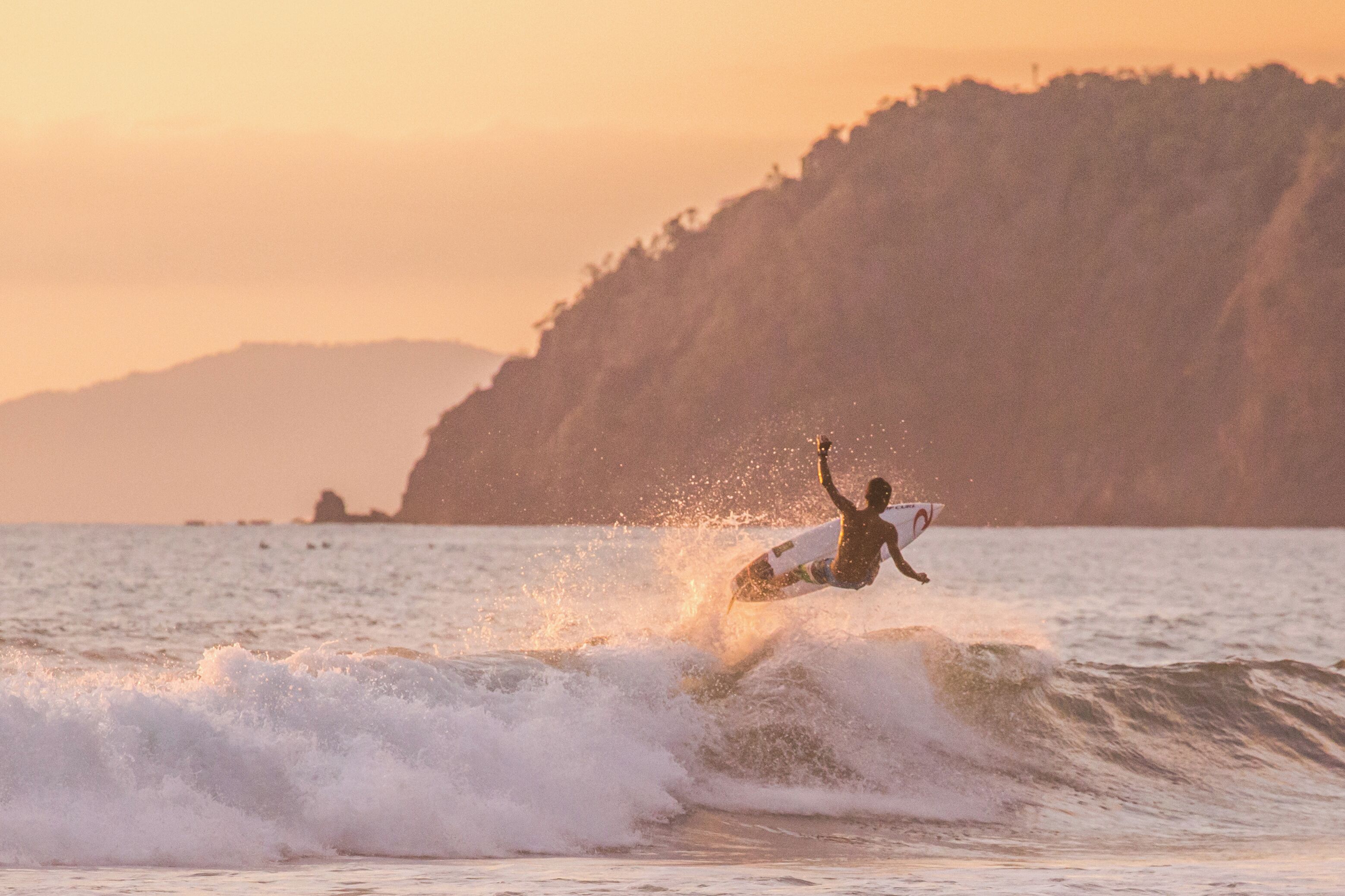 A surfer riding a wave with a coastal landscape in the background.