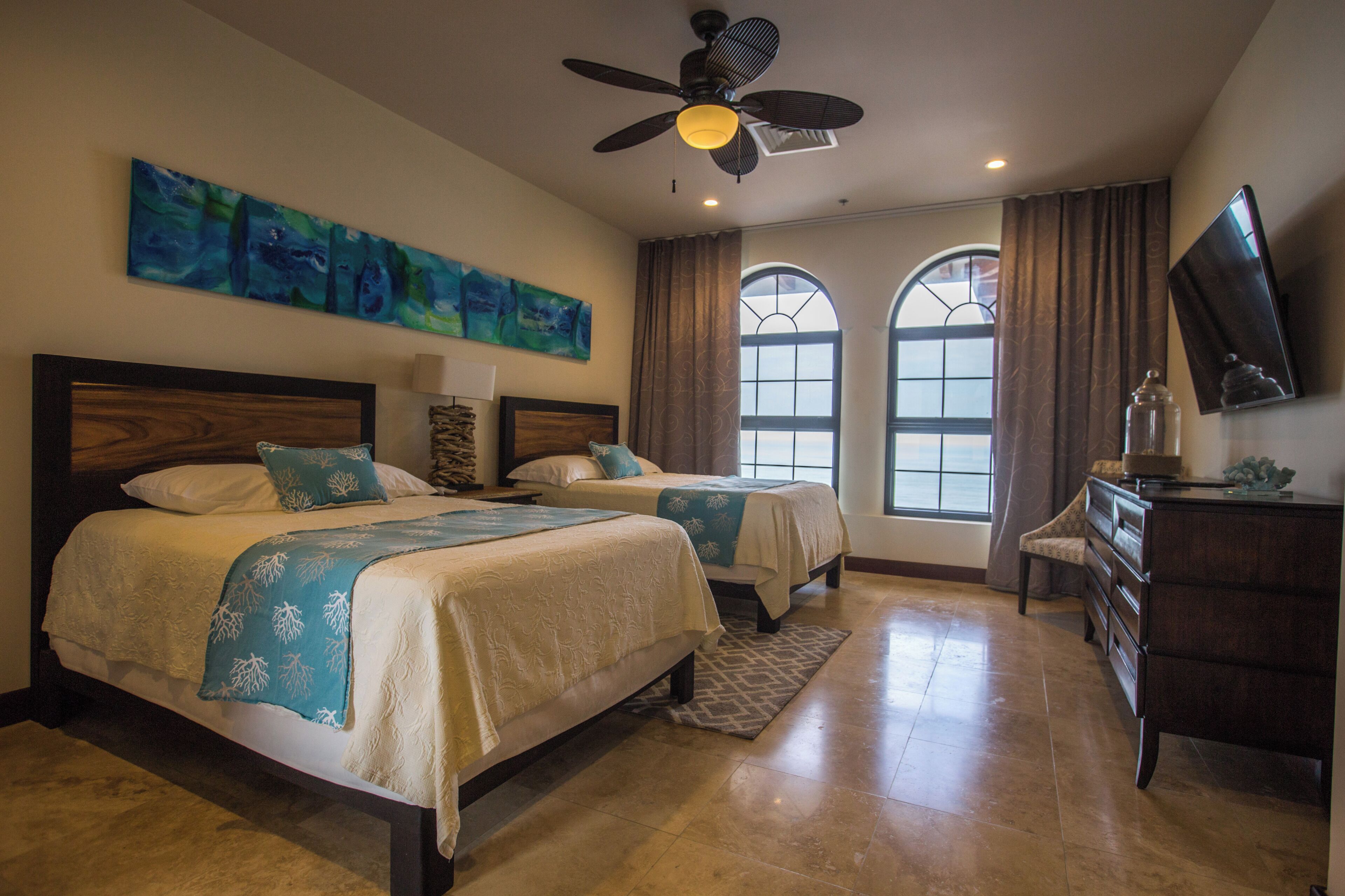 A bedroom with two beds, a ceiling fan, a dresser, and a TV on the wall.