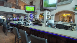 A bar area with multiple seating options, a television mounted above the bar, and a variety of bottles and glasses on the counter.