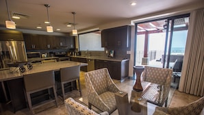 A modern kitchen with dark cabinets, a large island, and a dining area with patterned chairs.