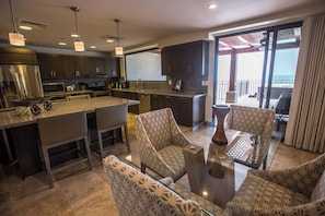 A modern kitchen with dark cabinets, a large island, and a dining area with patterned chairs.