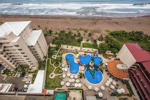 Un complexe hôtelier doté d’une grande piscine, offrant une vue sur la plage et comprenant plusieurs bâtiments.