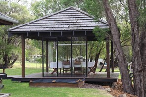 A covered outdoor seating area with a table and chairs, surrounded by trees. - Green Park - resort style rural retreat (Quindalup)
