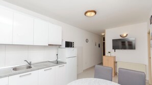 A modern kitchen with white cabinets, a stainless steel sink, and a microwave. There is a dining area with a table and chairs. - Apartments Anita Summer (Vodice)