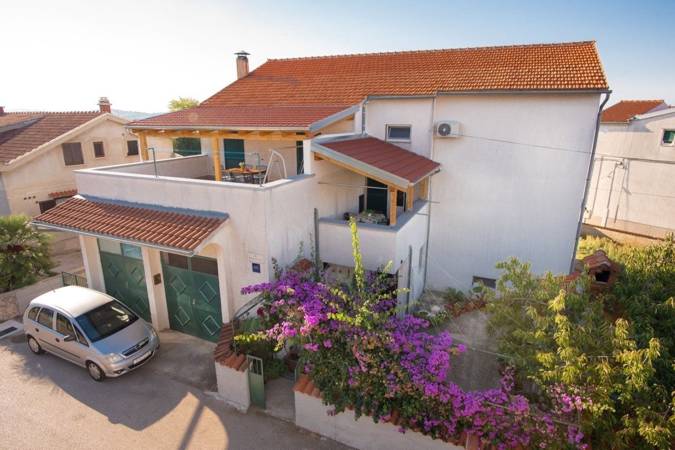 A two-story house with a red-tiled roof, a covered patio, and a car parked in front.