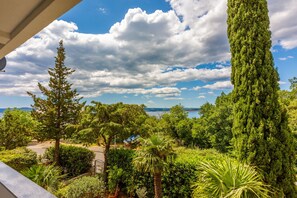 Un exuberante jardín con diversas especies de árboles y plantas, cielo despejado y vista al mar.