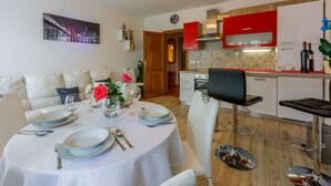 Une cuisine moderne avec des meubles rouges, un coin repas avec une table ronde pour quatre personnes, et un salon avec un canapé et un tableau au mur.