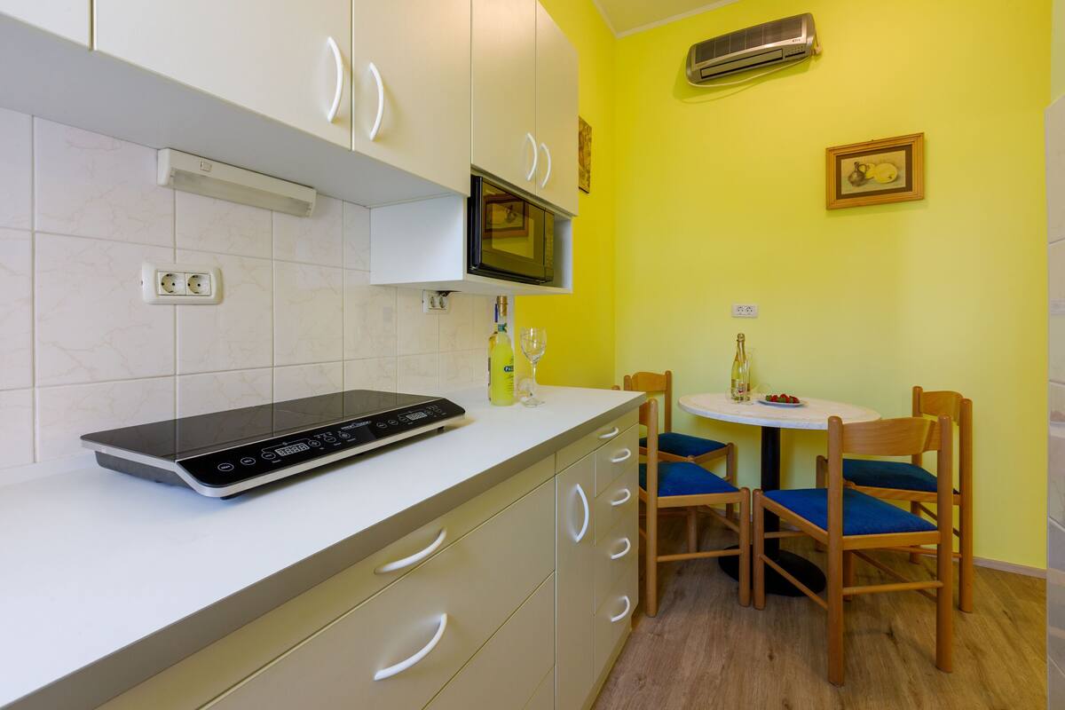 A compact kitchen with a built-in microwave, a modern induction cooktop, and a small dining area with two wooden chairs and a table.