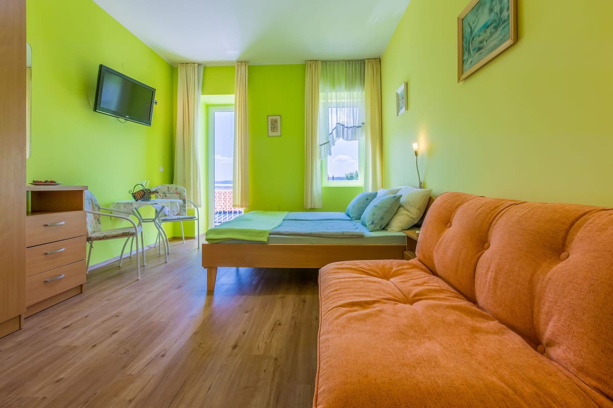 A room with a bed, a sofa, a TV, a desk, and a chair.