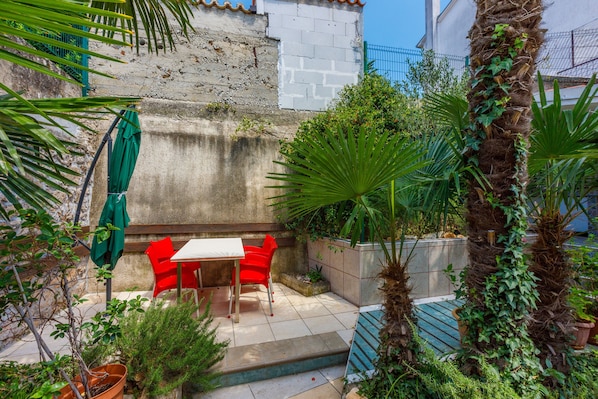 Un patio con mesa y sillas, rodeado de plantas y un muro de hormigón.