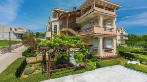 Un immeuble résidentiel à plusieurs étages, doté de balcons, d’un jardin avec différentes espèces de plantes et surplombant un ciel bleu dégagé.