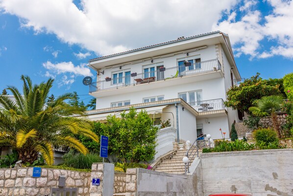 A two-story building with balconies, a stone wall, and a clear blue sky.