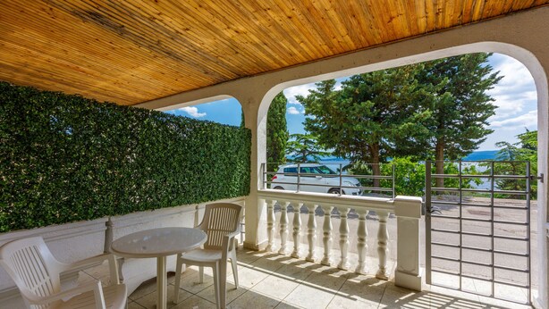 A covered outdoor seating area with a view of the sea and trees. - Apartments Lory (Dramalj)