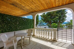 A covered outdoor seating area with a view of the sea and trees.