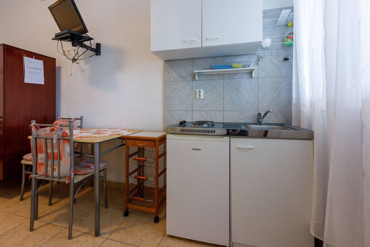 A compact kitchen with a sink, a small refrigerator, and a dining table with chairs.