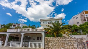 A two-story building with a balcony, a stone wall, and a clear blue sky. - Apartments Lory (Dramalj)
