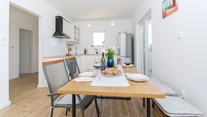 A modern kitchen with white cabinets, a stainless steel refrigerator, and a dining area with a wooden table and chairs. - Villa Dupla Kanica (Kanica)
