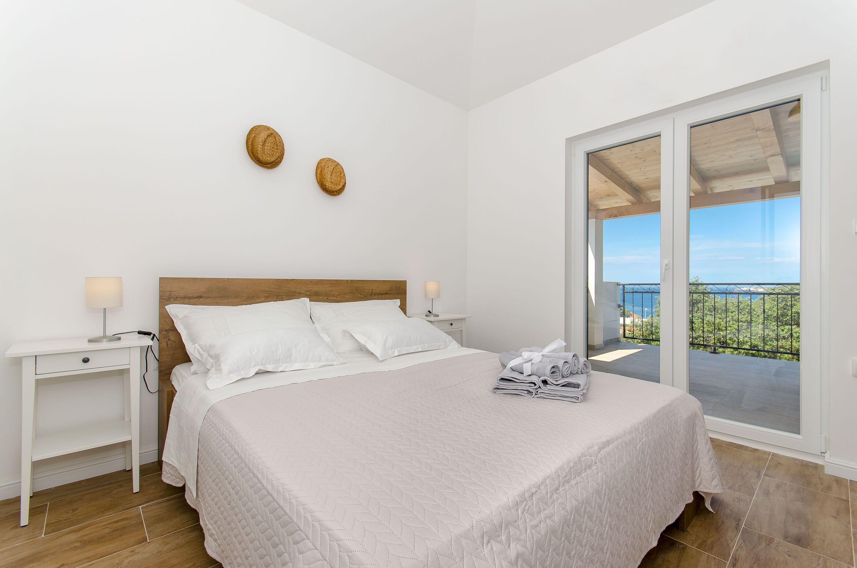 Un dormitorio con cama, mesitas de noche, cabecera de madera y vistas al balcón exterior por medio de una puerta corredera de vidrio.