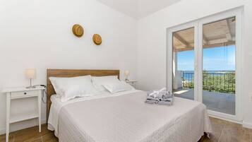 Un dormitorio con cama, mesitas de noche, cabecera de madera y vistas al balcón exterior por medio de una puerta corredera de vidrio.