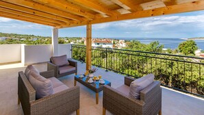A balcony with wicker furniture, a table with drinks, and a view of the sea and town. - Villa Dupla Kanica (Kanica)