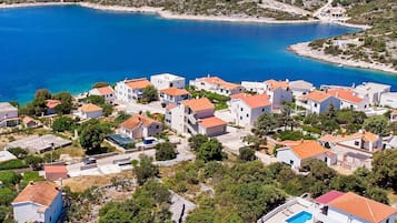 Un pueblo costero con edificios blancos y tejados rojos, un mar azul cristalino y una pequeña piscina.