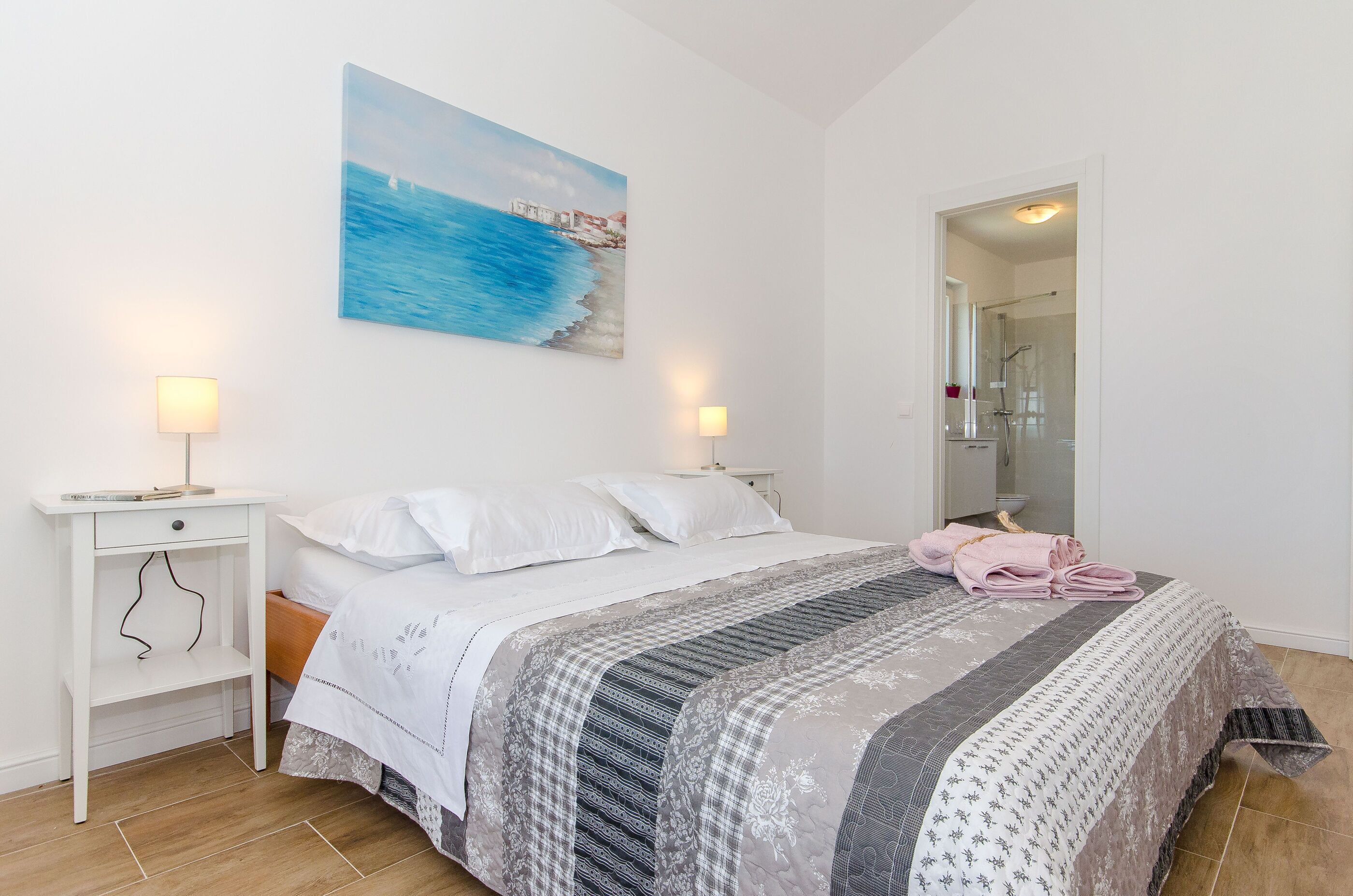 A bedroom with a bed, bedside tables, a painting, and a bathroom door.