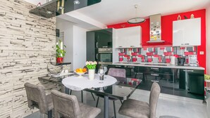 Una cocina moderna con armarios negros, una pared de acento roja y una zona de comedor con una mesa redonda y sillas.