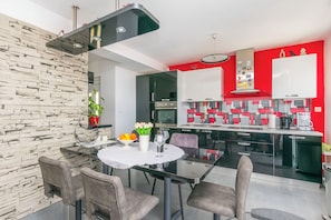 A modern kitchen with black cabinets, a red accent wall, and a dining area with a round table and chairs. - Apartment Marija (Omis)